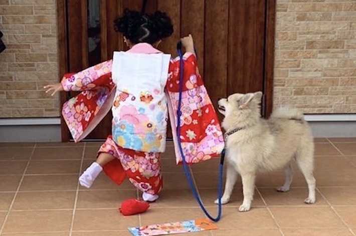 子どもが和服を着てドアを開けようとしている後ろ姿と、小型犬が寄り添う姿。