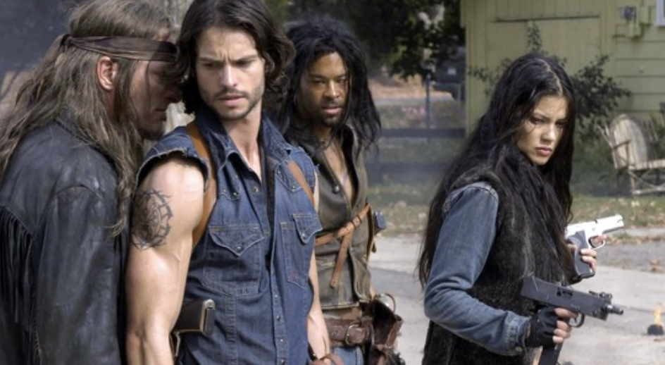 Four people stand in a gritty outdoor setting, wearing rugged outfits, preparing for action with focused expressions and weapons visible