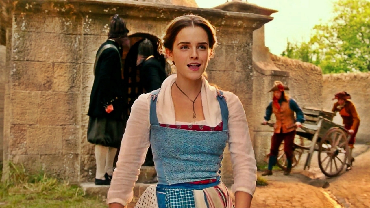 A person wearing a traditional 18th-century inspired dress walks in a village setting with stone architecture and workers behind