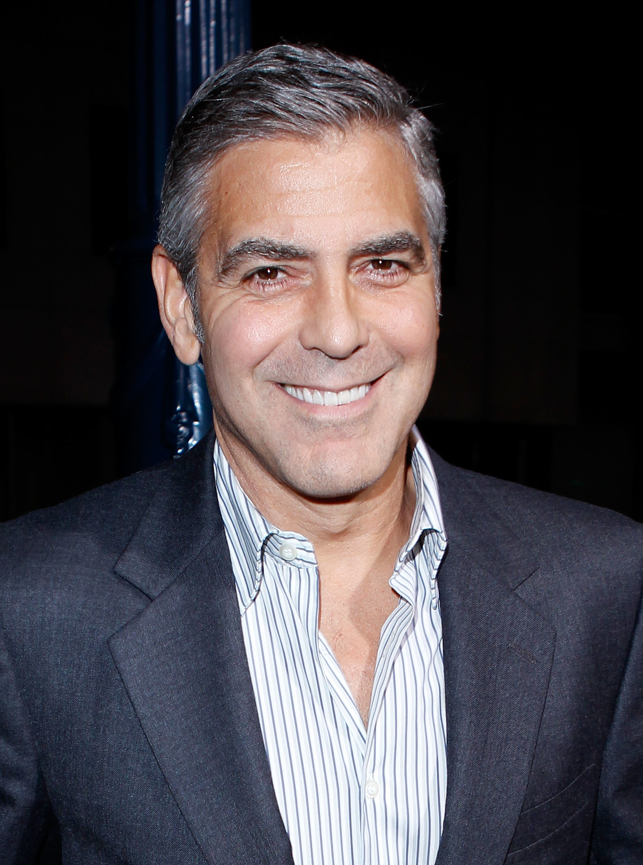 Person smiling, wearing a pinstripe shirt and dark suit jacket at a public event