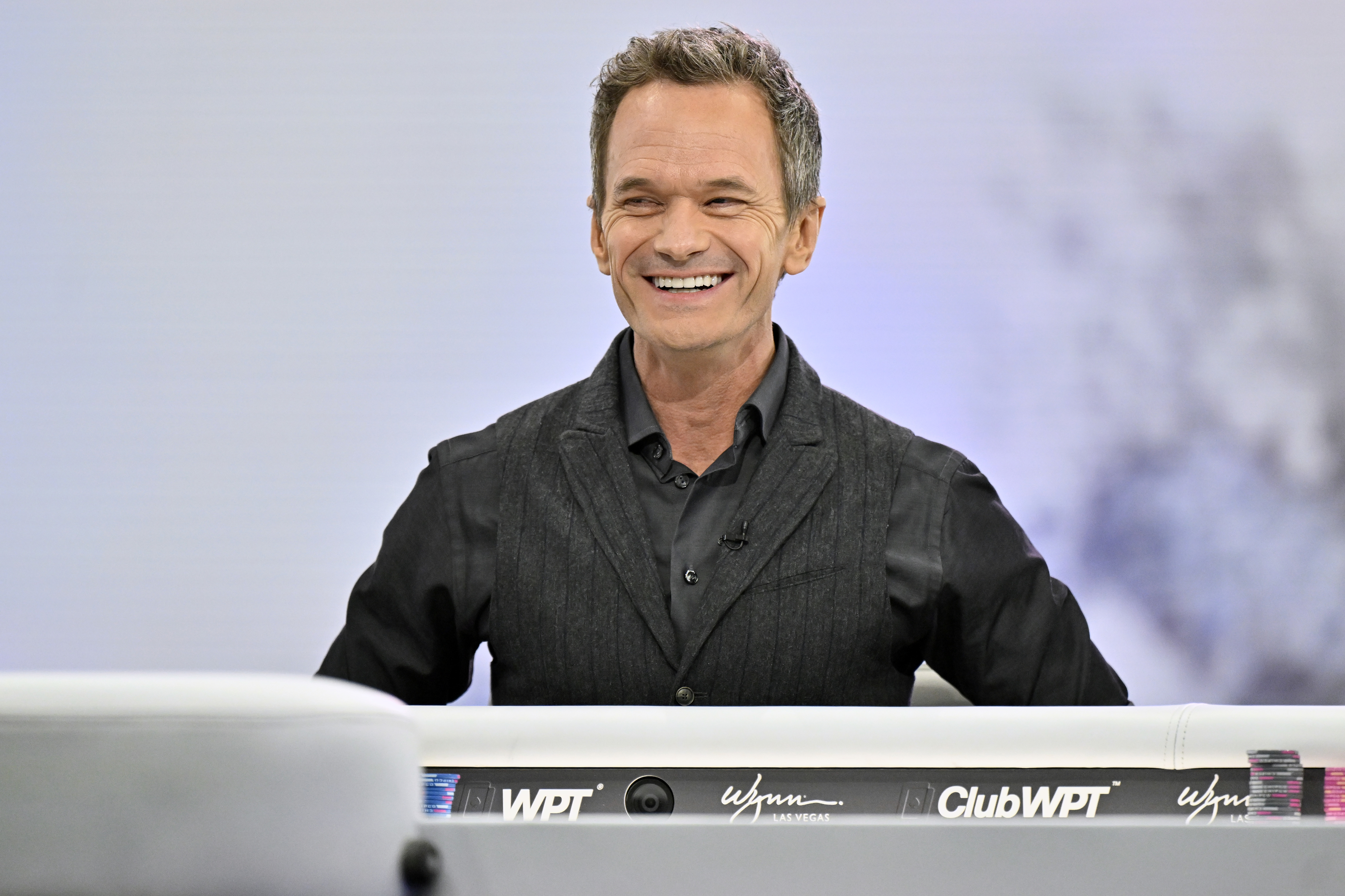 Smiling person in a dark suit vest and shirt, seated indoors at a ClubWPT event backdrop