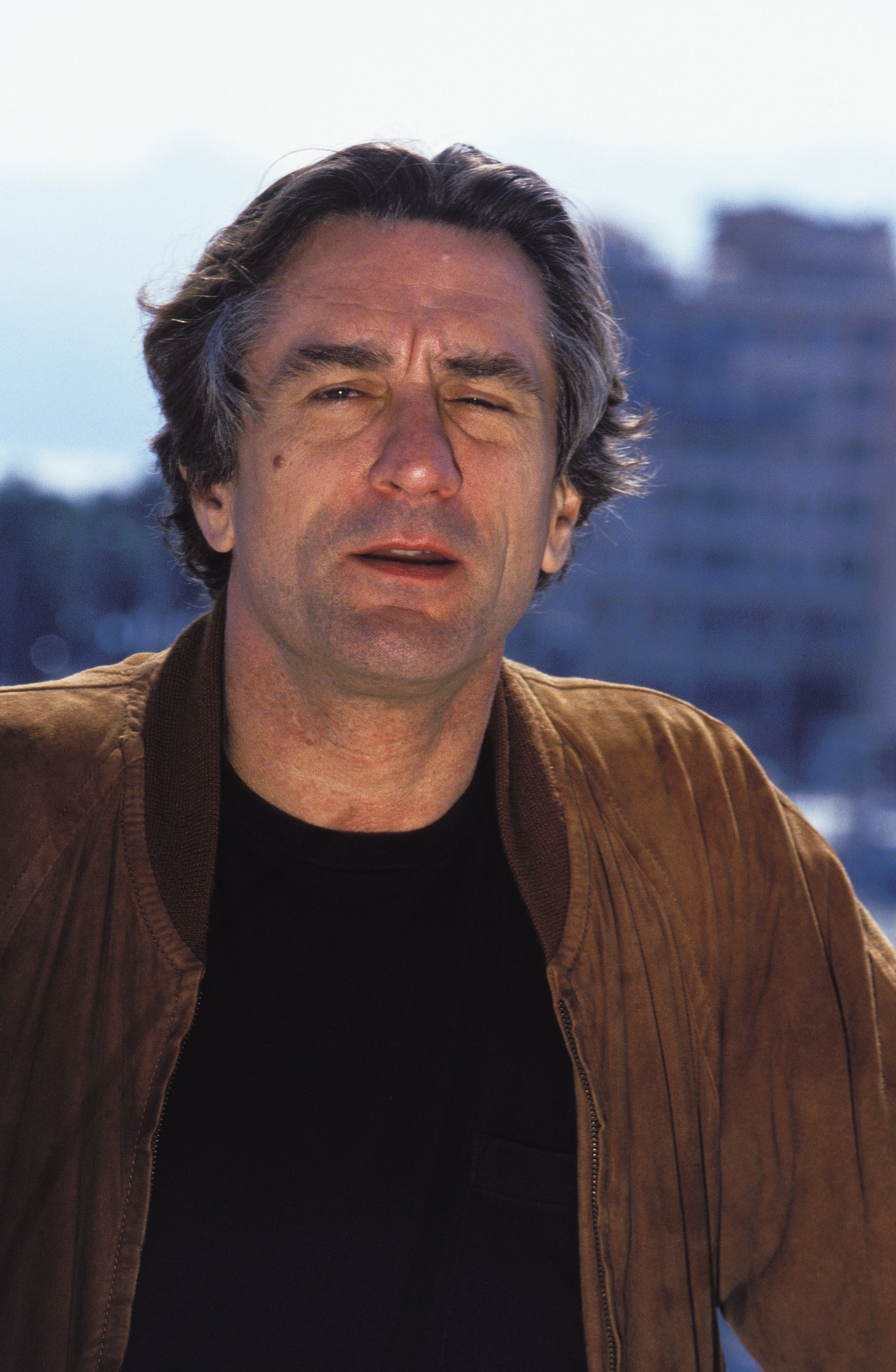 Person wearing a casual jacket and shirt, outside with a cityscape background