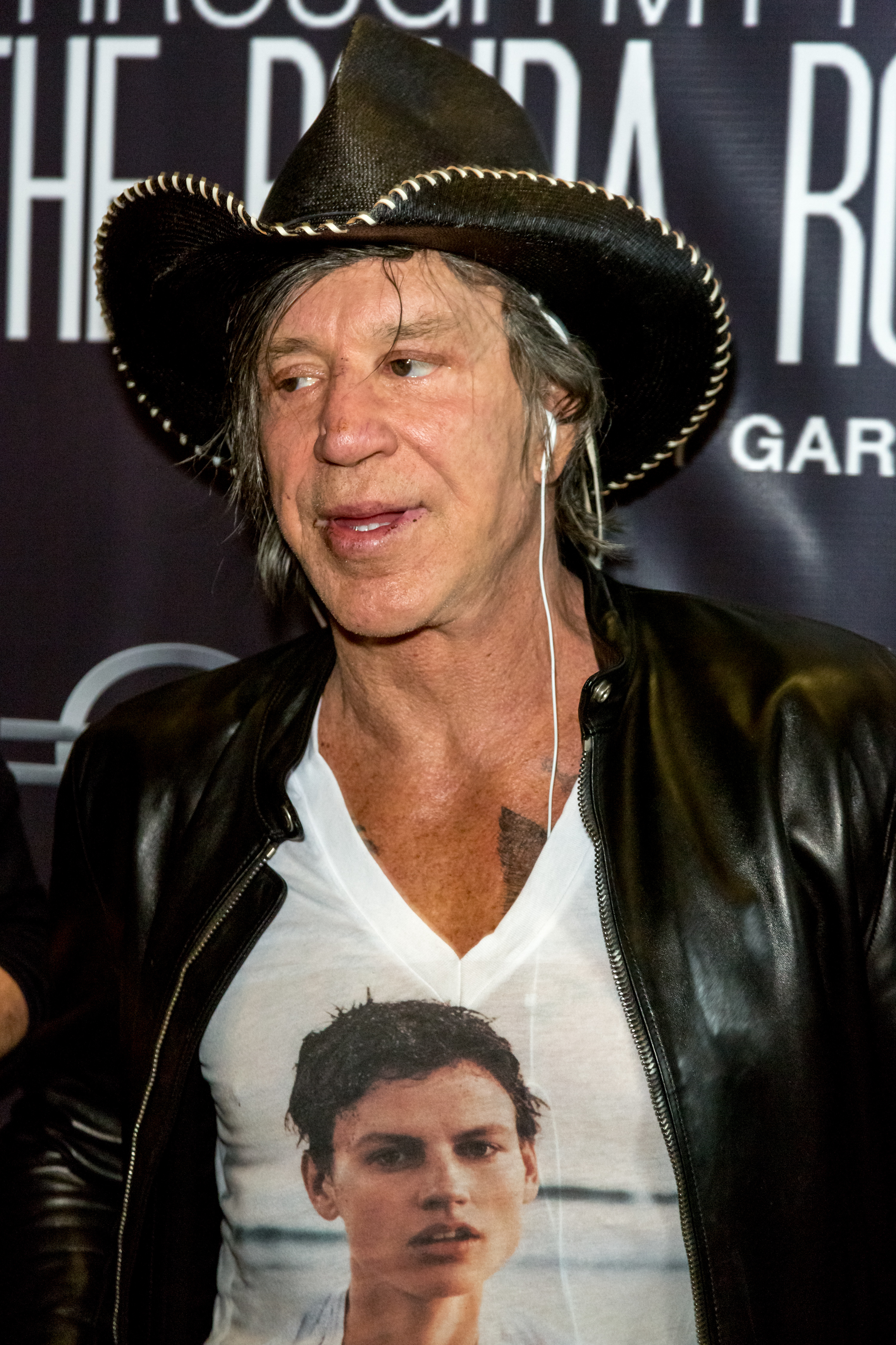 Mickey Rourke, wearing a cowboy hat, leather jacket, and t-shirt with a printed image, posing at an event