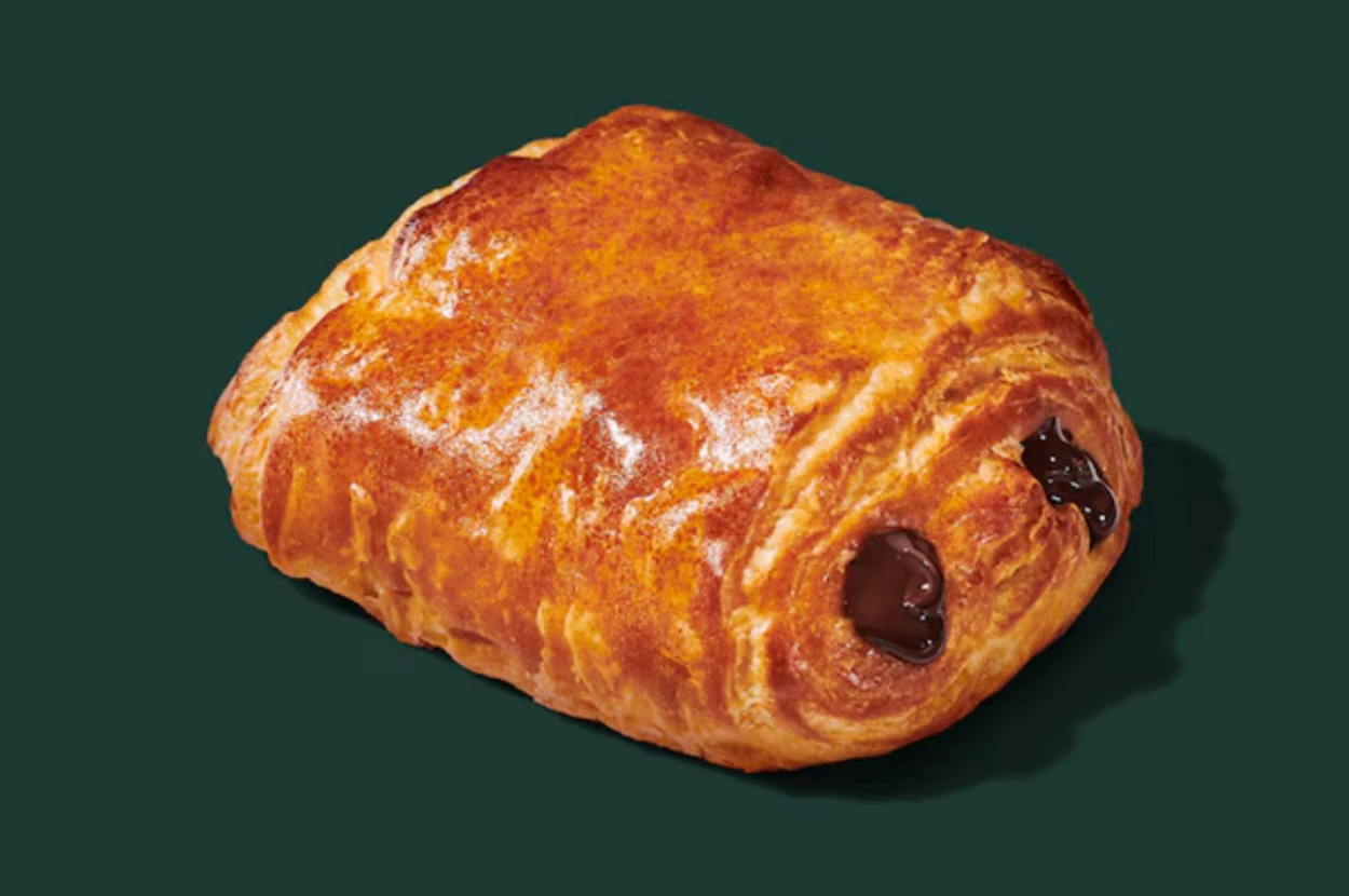 A flaky croissant with chocolate filling, resting on a solid dark background