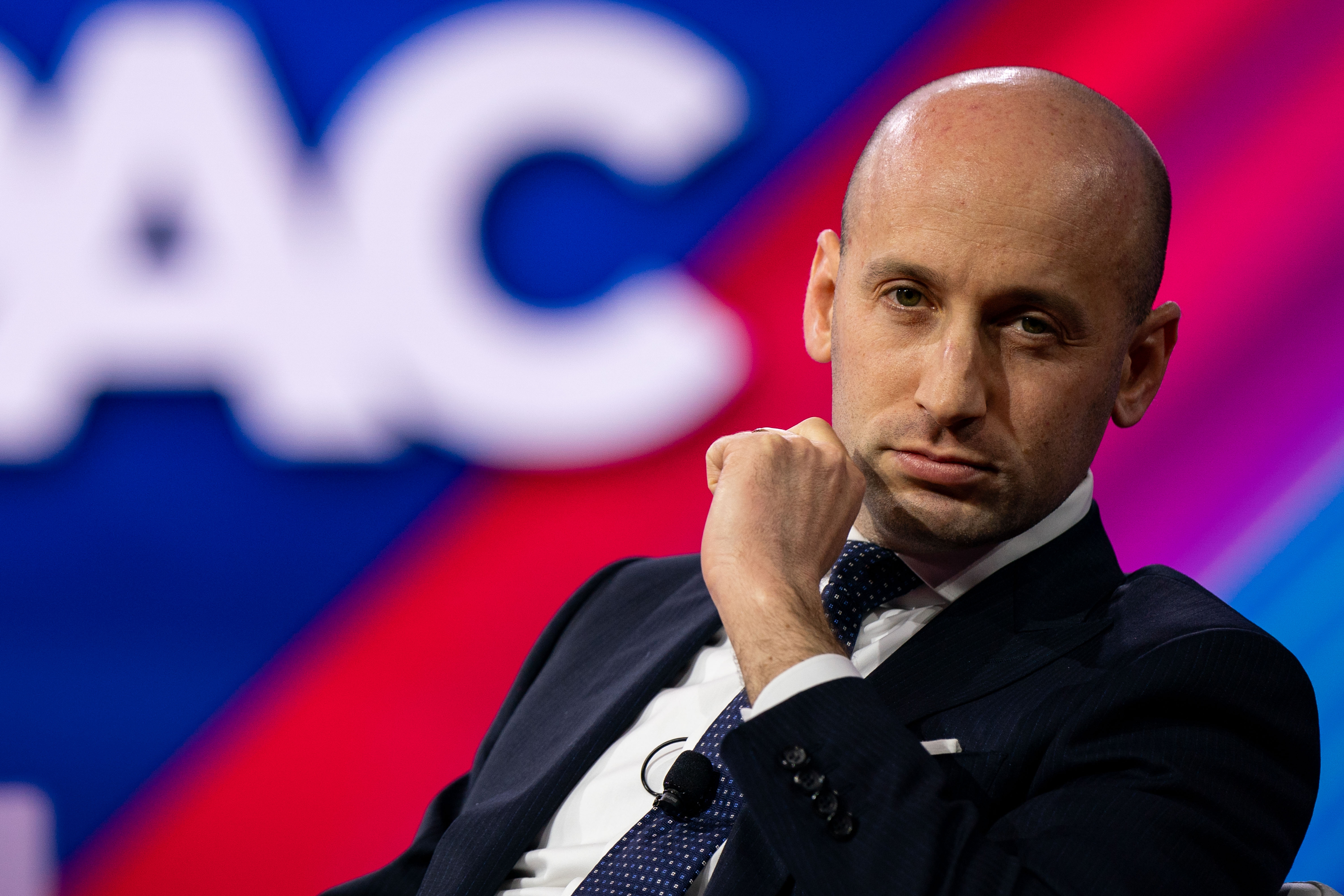 Person in a suit sits thoughtfully at an event with vibrant background signage