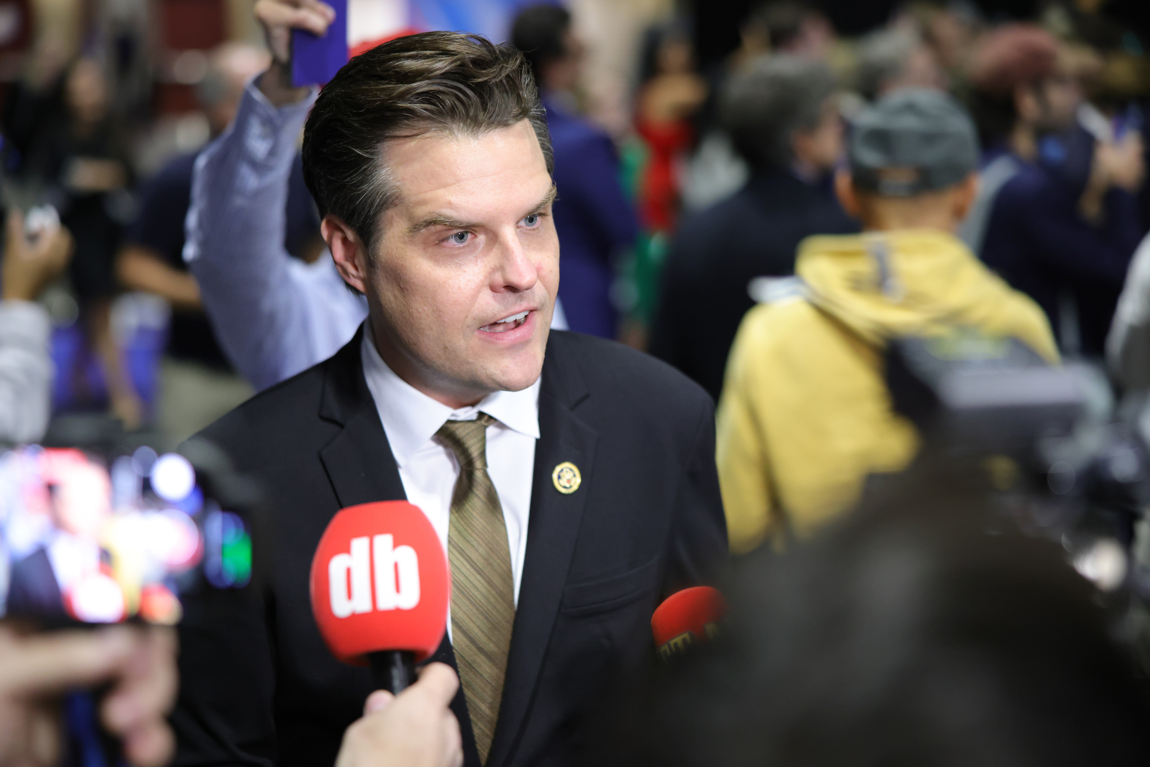 A person in a suit speaks to reporters surrounded by microphones at a public event