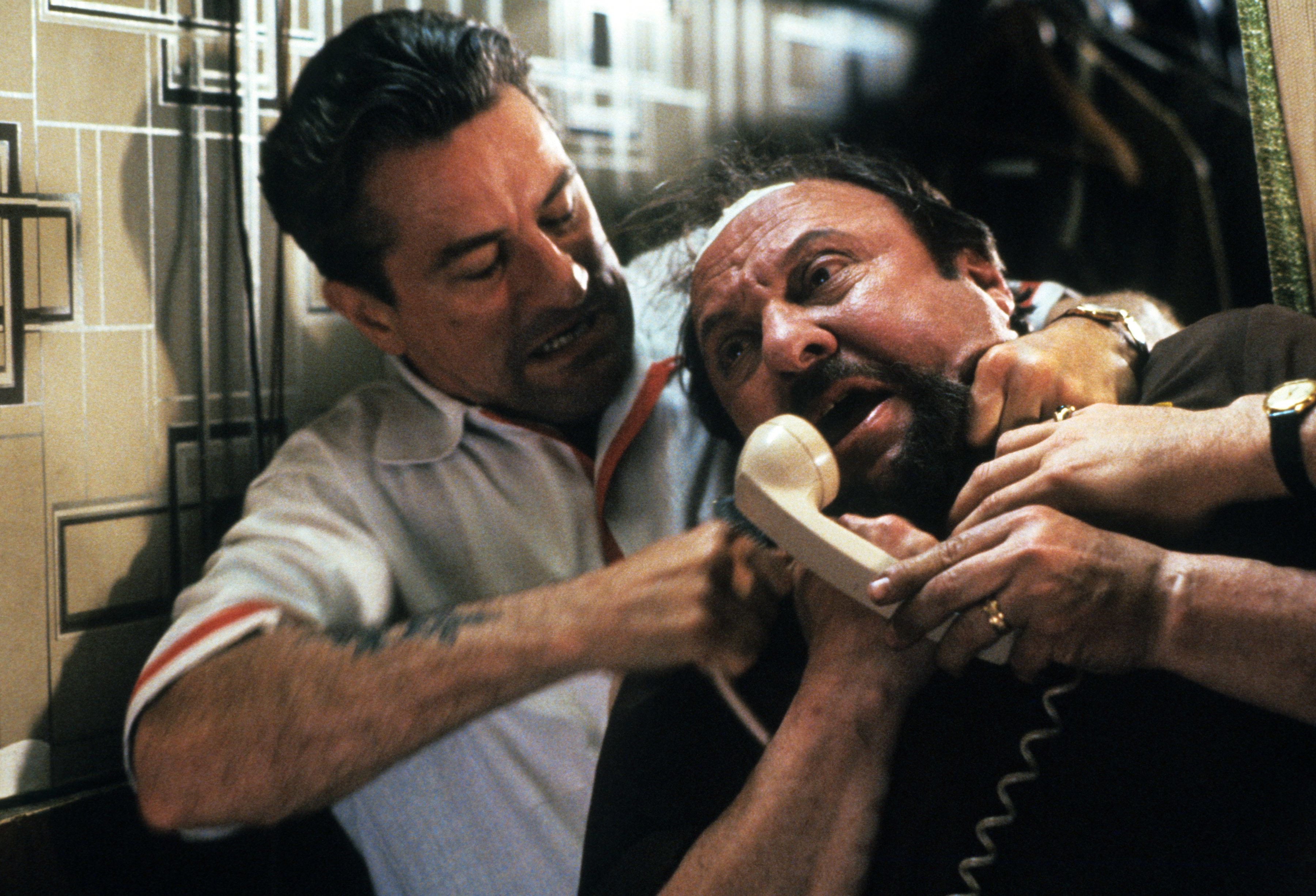 A tense scene from a movie where a man grips another man holding a phone, appearing confrontational