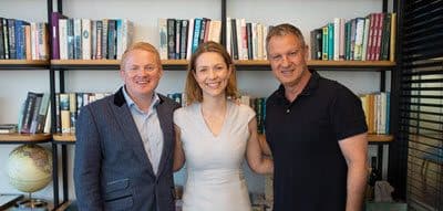 Erel N. Margalit and two other people stand together in a room with bookshelves behind them. The person on the left is wearing a suit, the person in the middle is in a light dress, and the person on the right is in a dark polo shirt. They're all smiling at the camera.