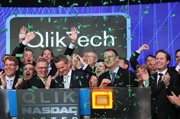 A jubilant group in suits celebrates with green confetti in front of a QlikTech sign at a Nasdaq event, capturing the perfect moment for their homepage.