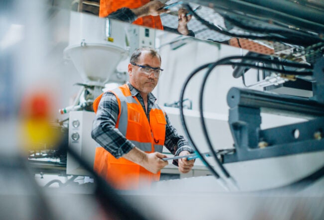 Man working with machines in a factory to show how robots are taking over low-skilled jobs