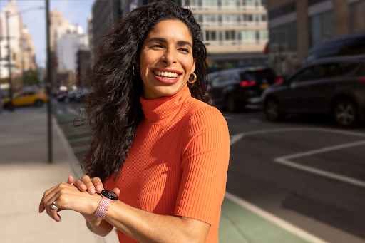 The smartwatch user is standing on the pavement in a city-centre area and smiling while looking in the direction that the Google Maps watch is navigating towards.