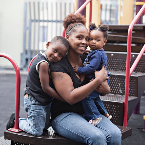 A woman smiling and hugging her kids on a playground.