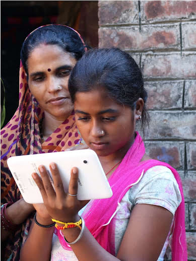 A young girl uses a Google Pixel, while an older woman stands behind her, watching closely with a caring expression.