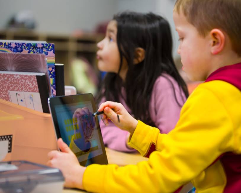 A child is drawing on a screen while another child is looking on.