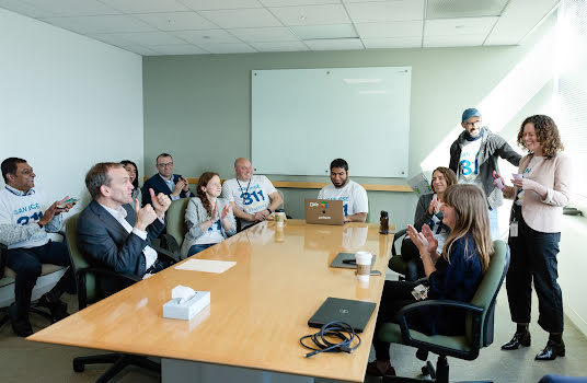 A large group of people in a conference room smiling and clapping.