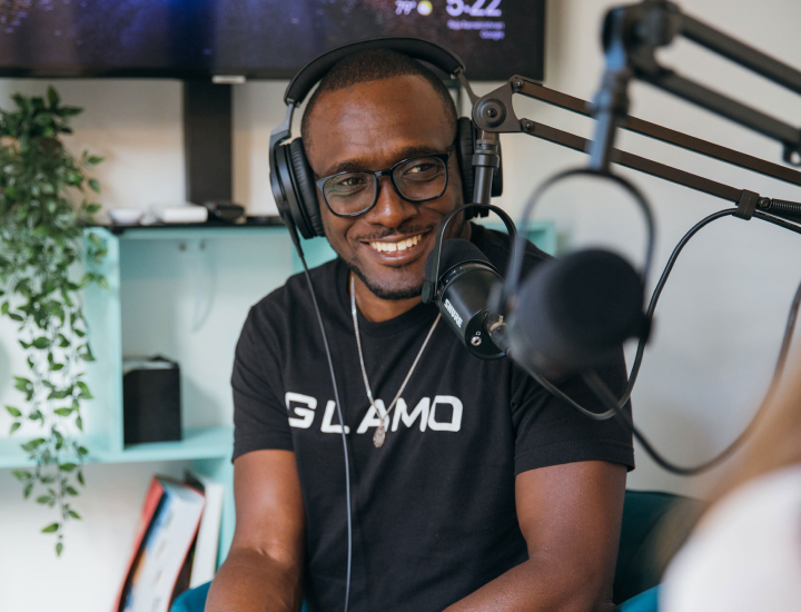 A man wearing headphones speaking on the mic and smiling