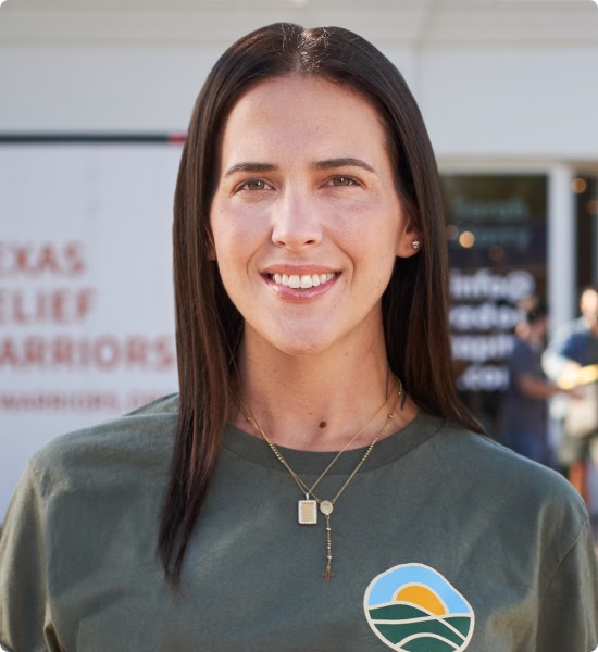 Cara in front of semi-trailer trucks being loaded with supplies by volunteers.