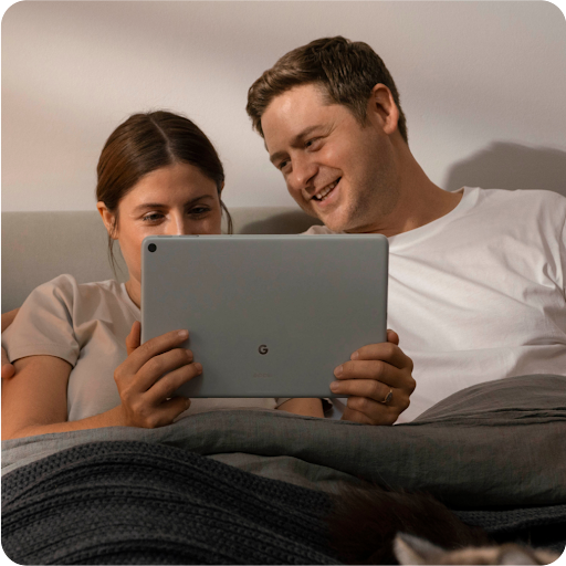 Two people relaxing in bed and smiling watching entertainment on their tablet.