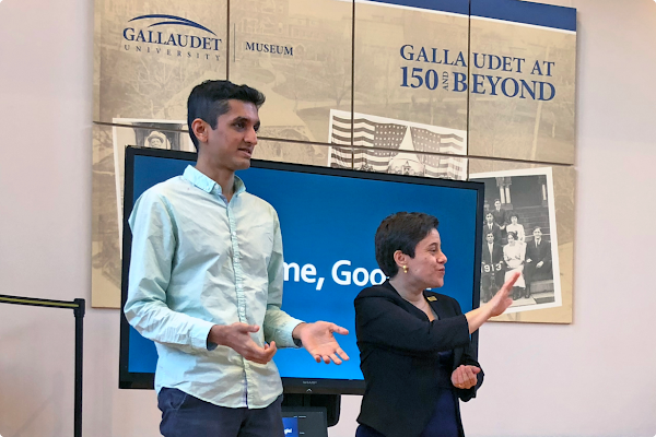 Sagar Savla speaks with a Gallaudet University sign behind him. Standing next to him is a female sign language interpreter.