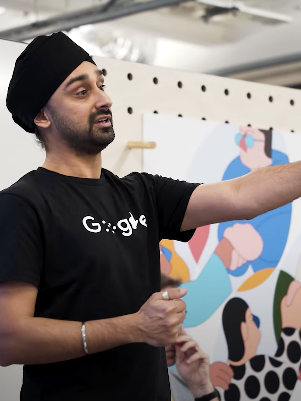 A bearded man with a black turban wears a shirt with Google’s disability logo.