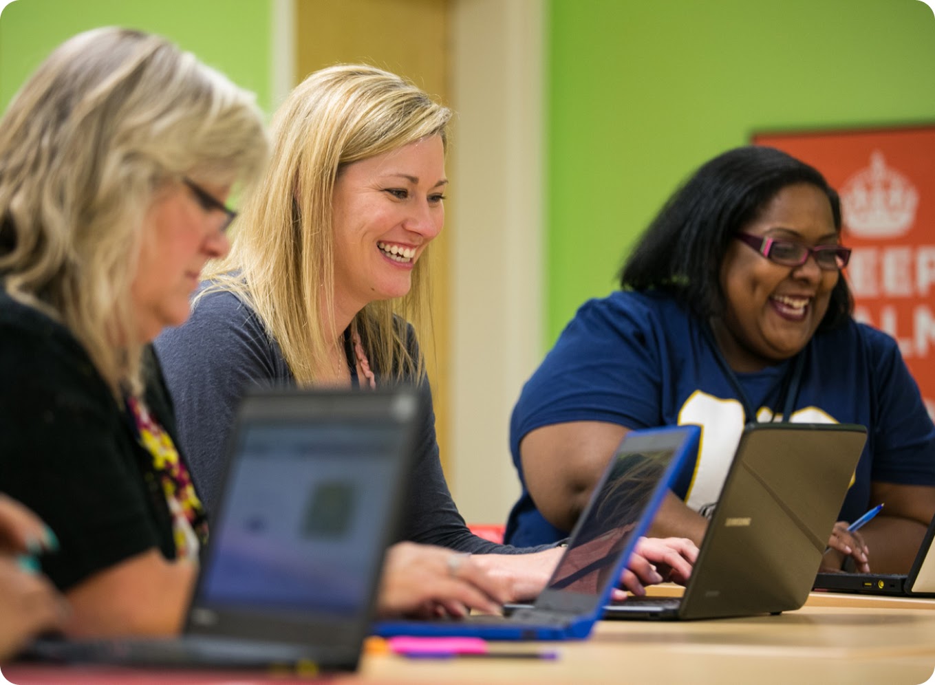 A group of people smile as they work together on laptops in a shared workspace.