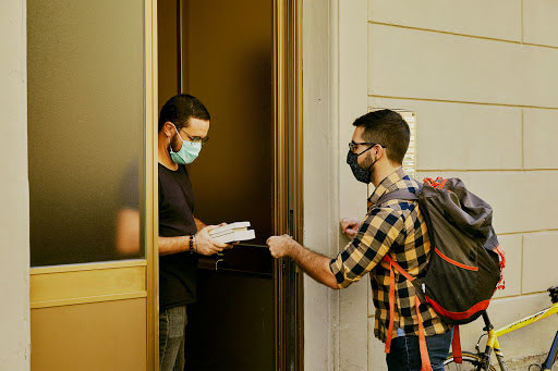 He delivers a handful of books to a masked customer through his front door