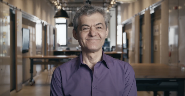 Dimitri Kanevsky faces the camera sitting down and smiling. He has short gray hair and is wearing a purple shirt.