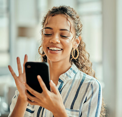 A Black female office employee wearing golden earrings and a striped button up shirt smiling while using a corporate mobile device.