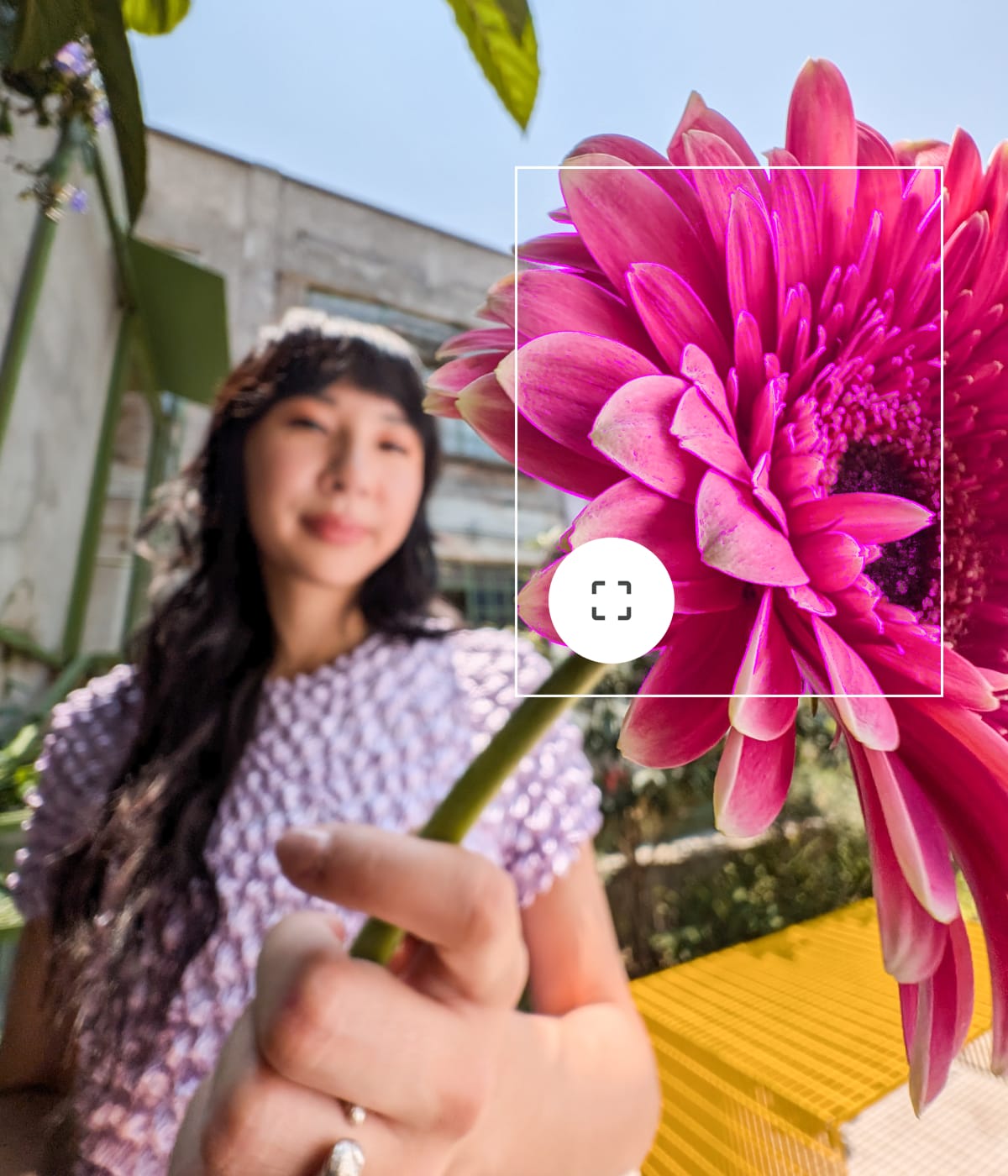 A person stands out of focus holding a bright pink flower to the camera. The overlaying interface focuses on the flower.