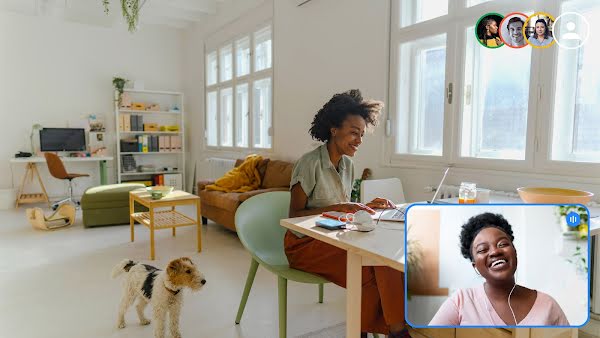 Dos mujeres participan en una videollamada de equipo. Una está sentada en un escritorio con un perro a su lado. La otra se ríe en la ventana de la videollamada.