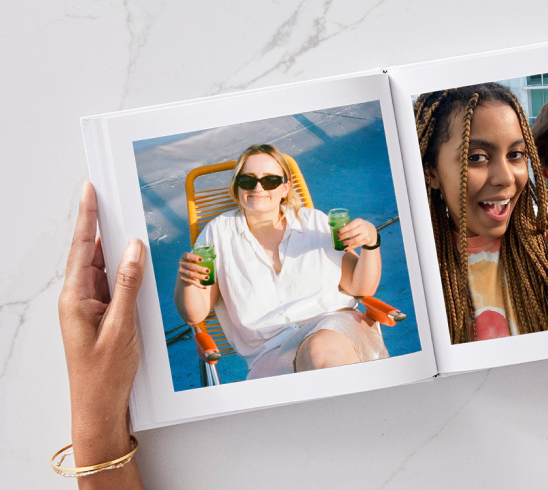 Hands holding a photo book opened to a page featuring a woman holding two drinks in a beach chair.