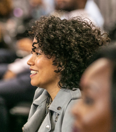 A woman with short, curly hair smiling and attending the conference with other people