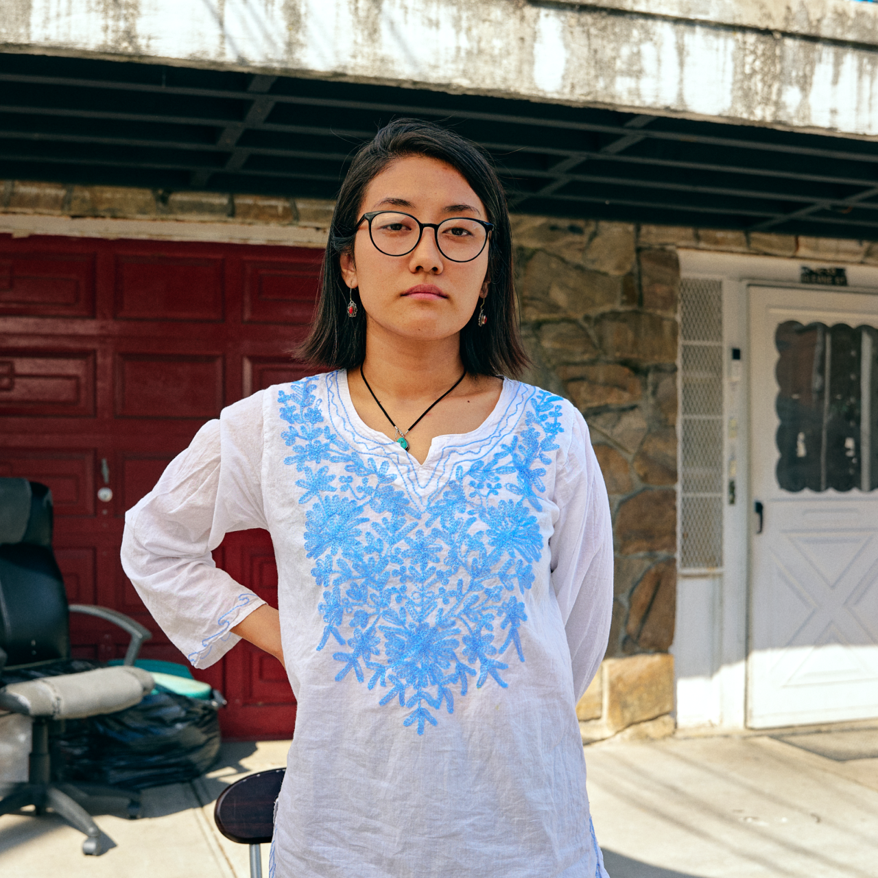 East Asian woman standing in a blue and white shirt with glasses on.