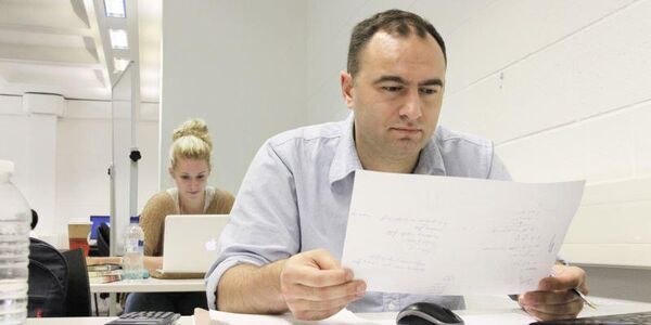 A man at a desk reading a from a piece of paper.