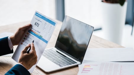 Person holding credit report in front of computer 