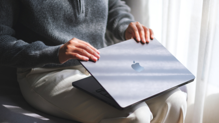 person opening a macbook on their lap, booting up computer