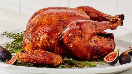 A roast turkey on a white plate with figs and herbs around the bottom.