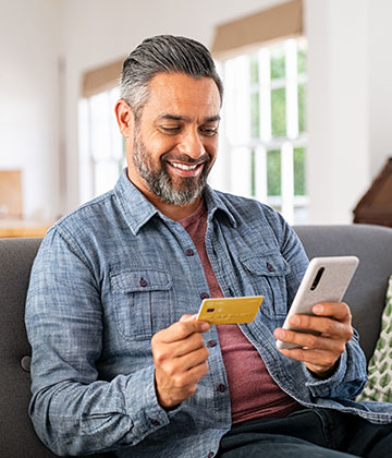 Man smiling, holding credit card while purchasing an item on his phone