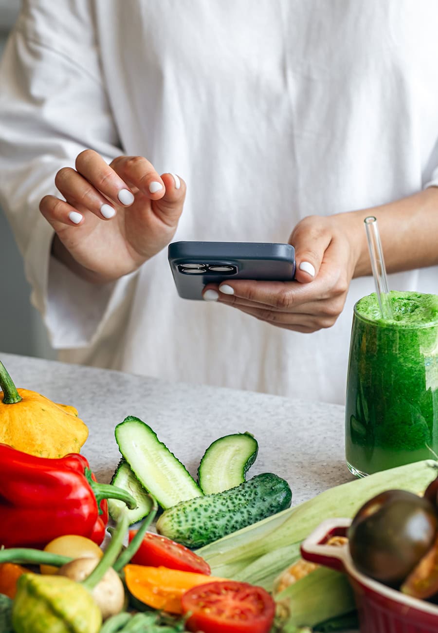 Woman holding mobile phone looking at fresh food on bench with green smoothie.