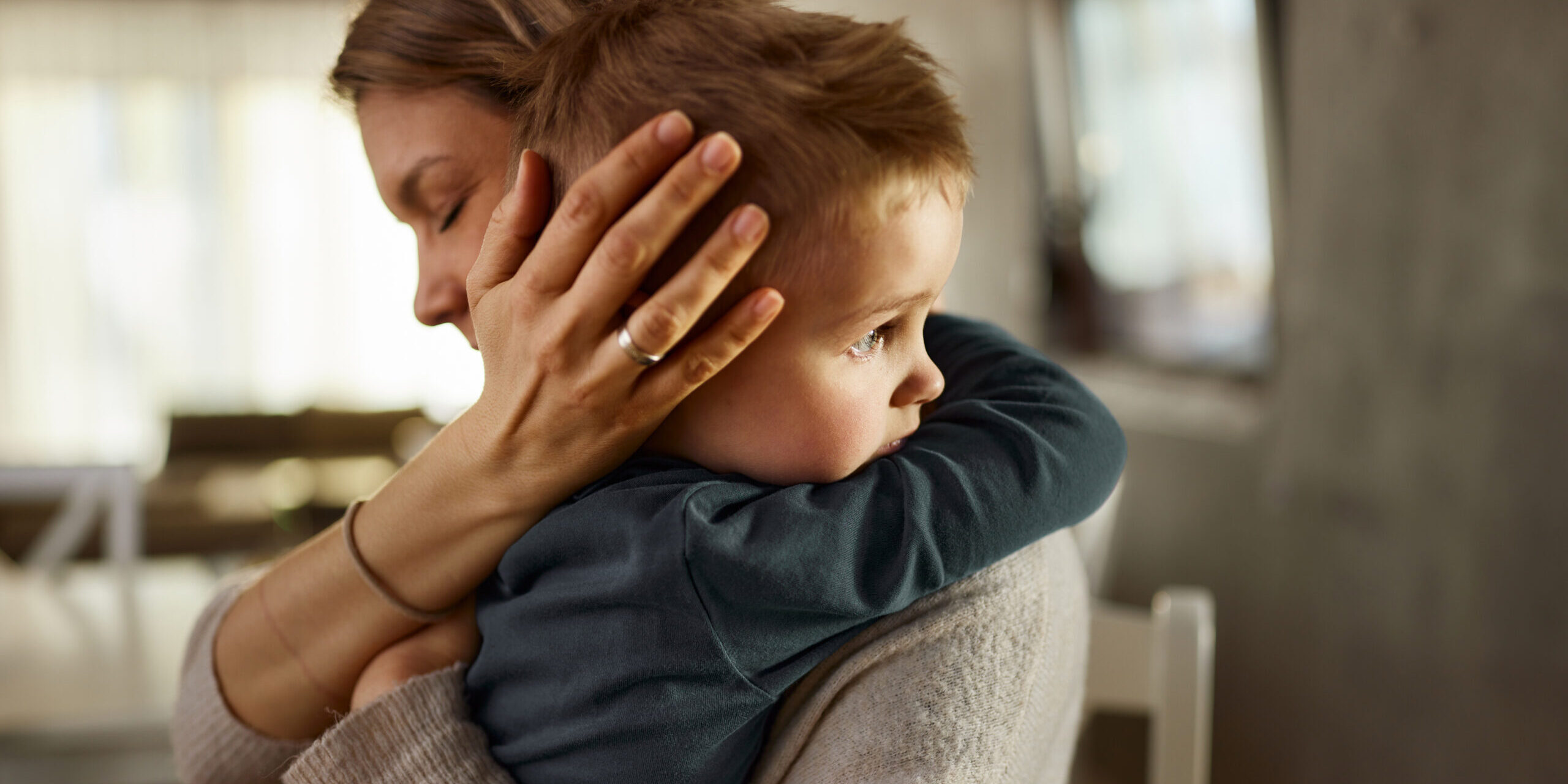 Single mother consoling her sad little boy at home.