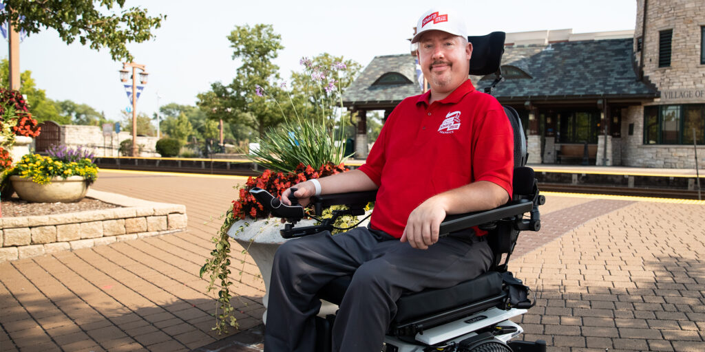 Jeremy sits in a power wheelchair at a brick paved intersection