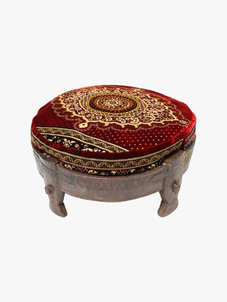 Round ottoman with a hand carved teak base and a red velvet upholstered cushion embroidered with an Indian design.