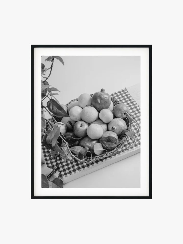 Framed black and white photograph of a fruit bowl filled with with apples pomegranates and oranges on top of a checkered...