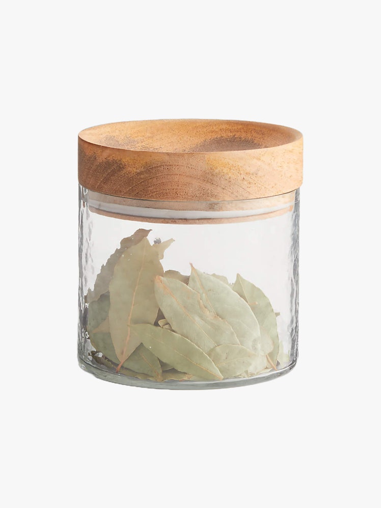 Small glass canister with wooden lid that has bay leaves inside.