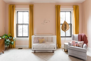 pinkwalled baby girl nursery bright ochre drapes parted over two windows on either side of white crib at center gray...