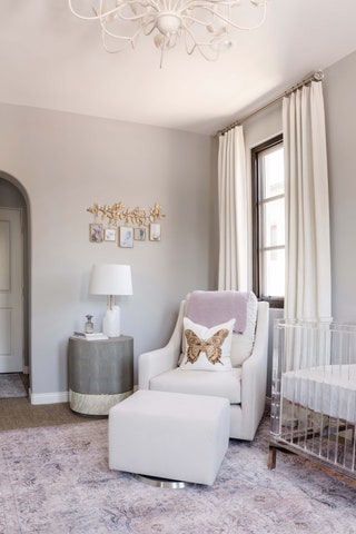 sculptural white chandelier overhead gray walls white drapes parted window at corner white armchair and matching ottoman...