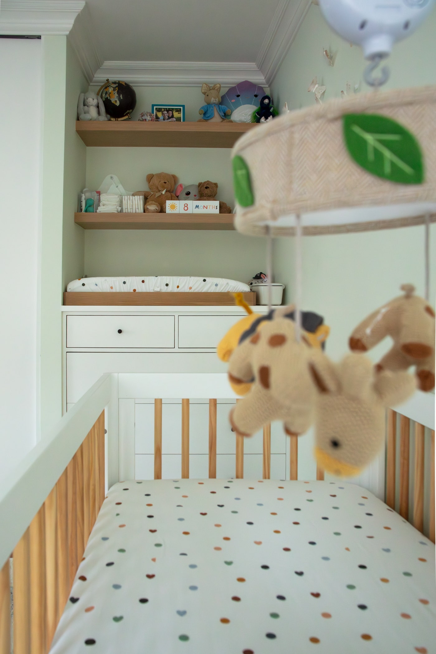 in blurred focus in foreground stuffed animal mobile in focus white crib with brown lightwood bars white crib sheets...