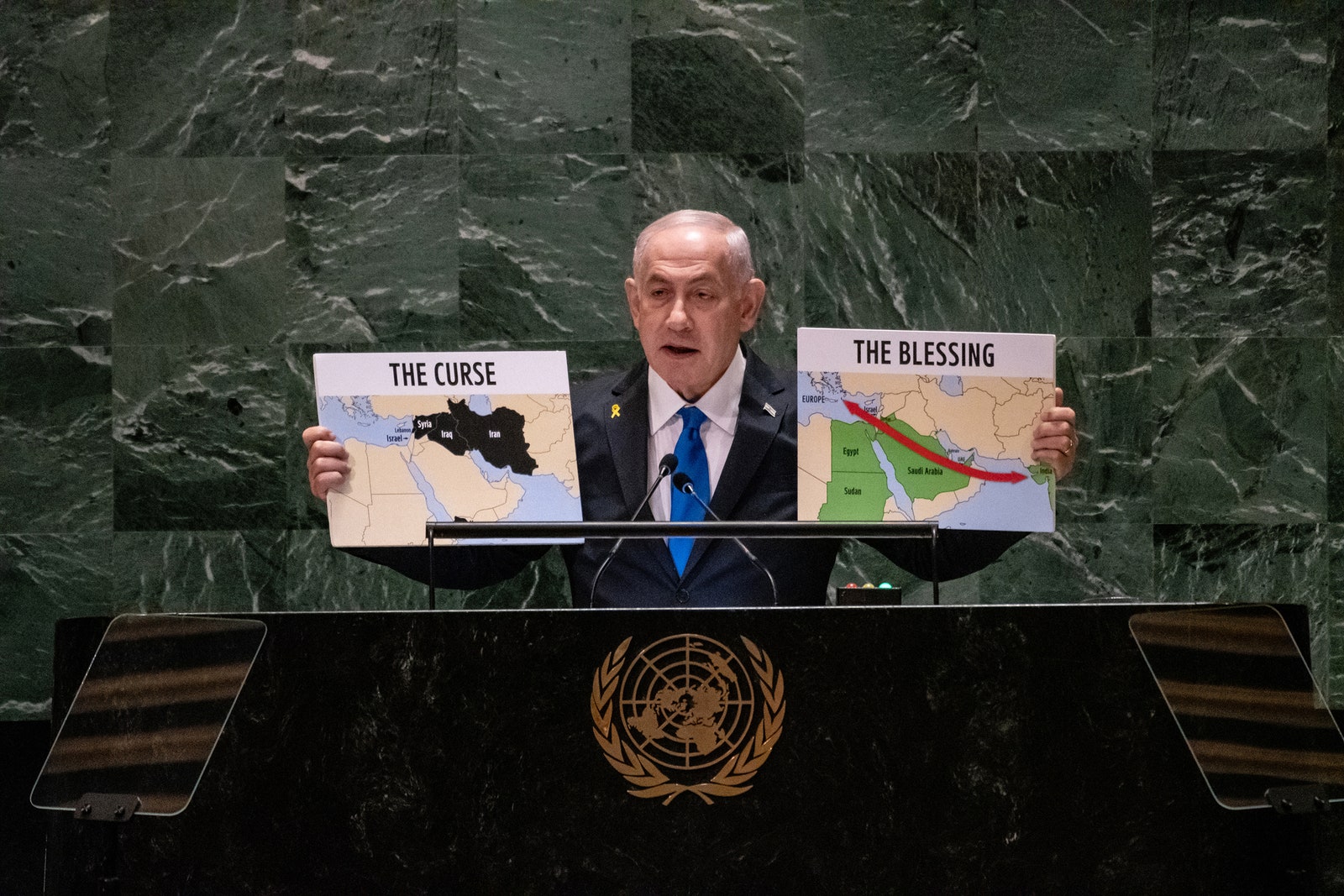 Israeli Prime Minister Benjamin Netanyahu holding up two signs one says THE CURSE and the other says THE BLESSING.