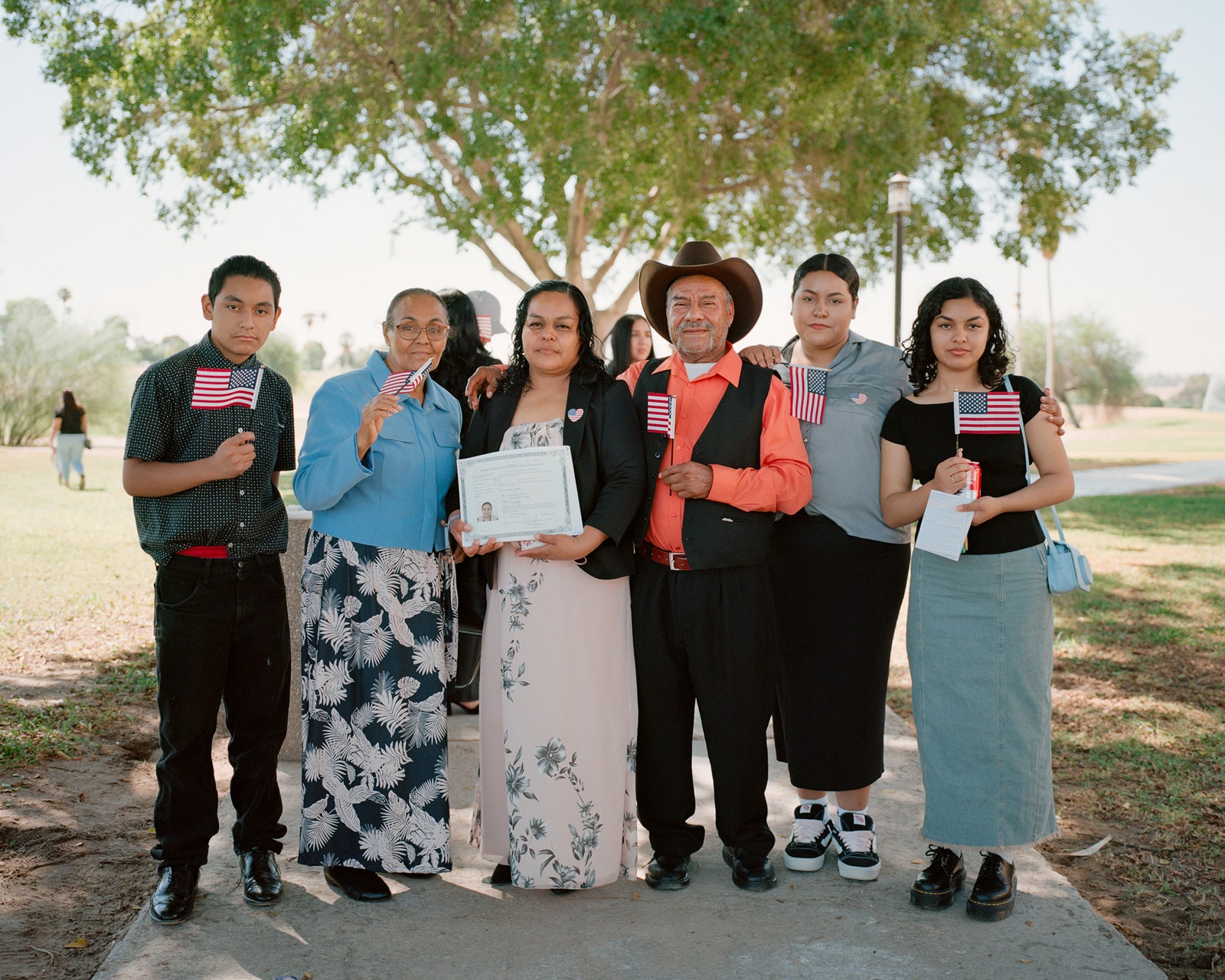 People stand side by side with small American flags in hand. A person in the middle holds a certificate.