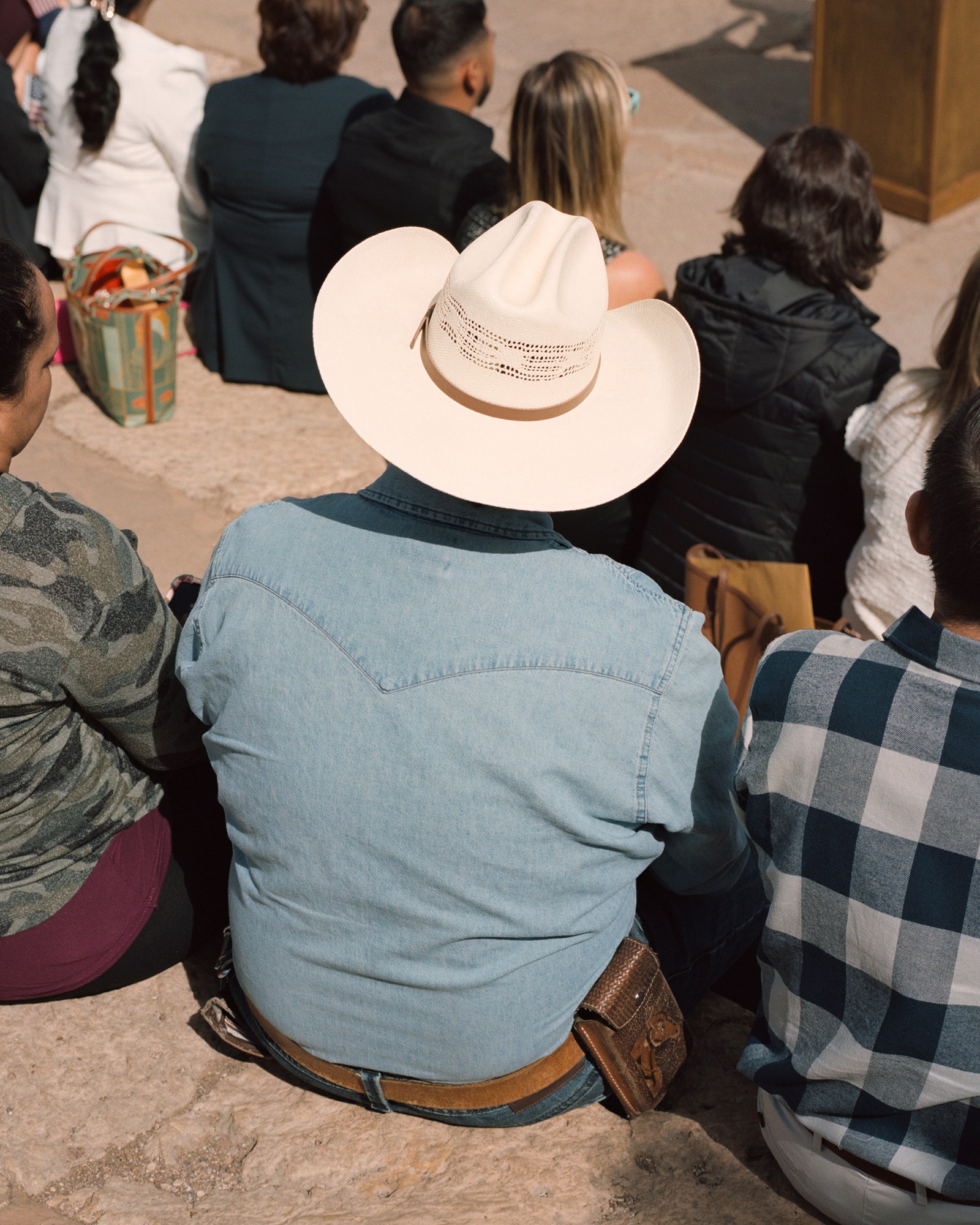 A person photographed from behind they are wearing a denim shirt and a cowboy hat.